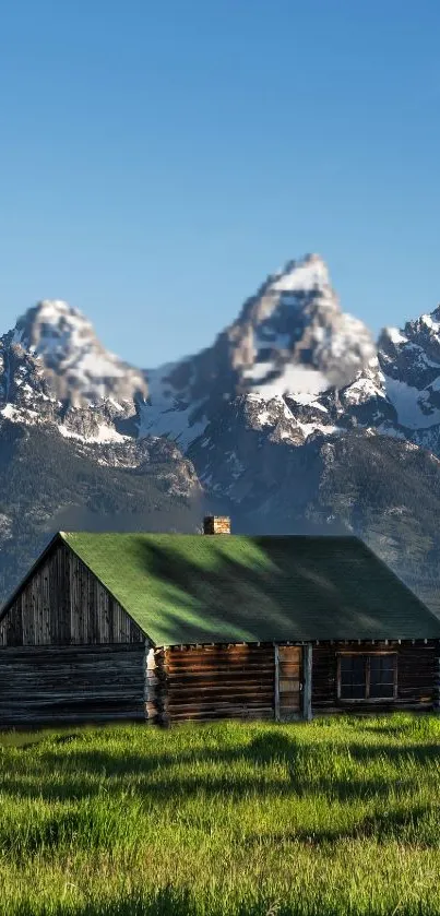 Rustic cabin with mountain backdrop under blue sky.