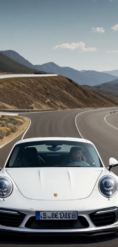 White sports car driving on a scenic mountain road with blue sky and clouds.