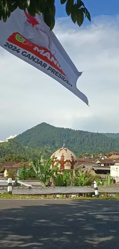 Scenic mountain and town with a flag waving under a clear blue sky.