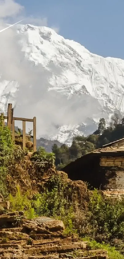 Scenic mountain path with a stone house and snowy peaks under a clear sky.