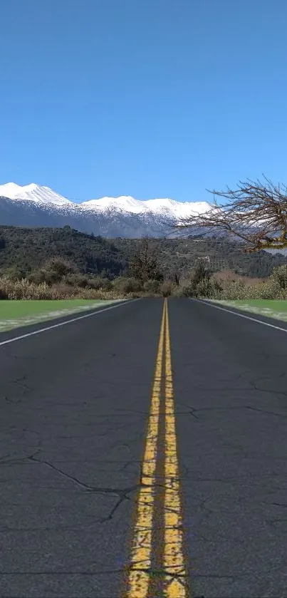 Mountain road leading to snow-capped peaks under a blue sky.