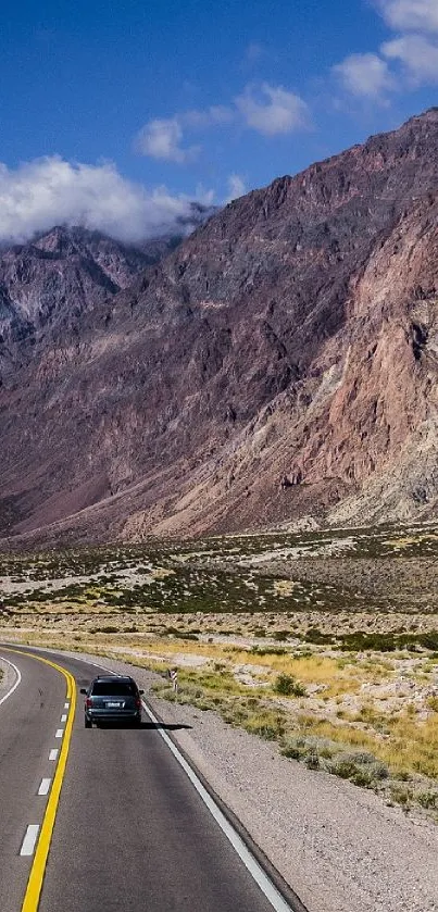 Car journeying through vast mountain landscape under blue sky.