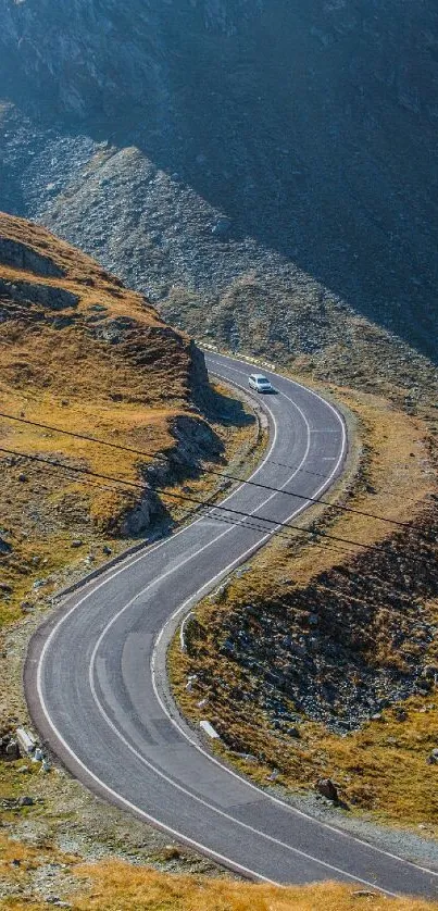 A car drives down a winding road through scenic mountain terrain under blue skies.