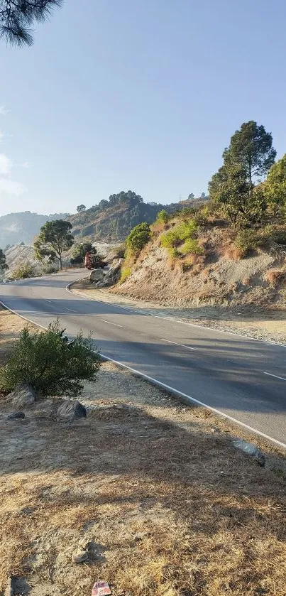 Scenic road through mountains with trees under a clear blue sky.