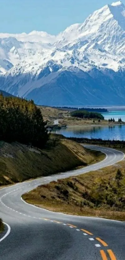 Winding road leading to snow-capped mountains and serene blue lake.