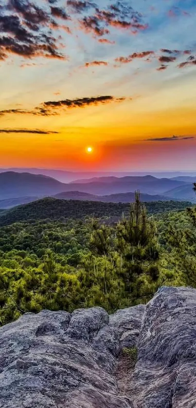 A stunning sunset over lush green mountains with a rocky foreground.