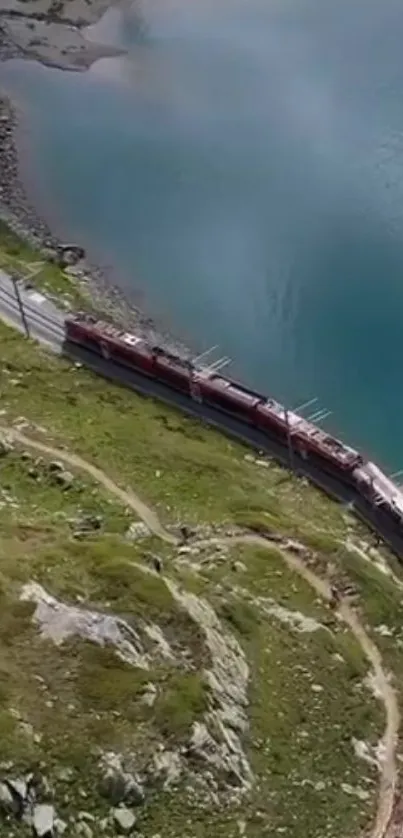 Aerial view of a train winding through mountains by a blue lake.