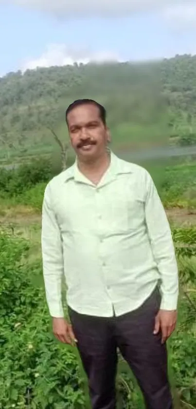 Man stands in lush green landscape with hills in background.