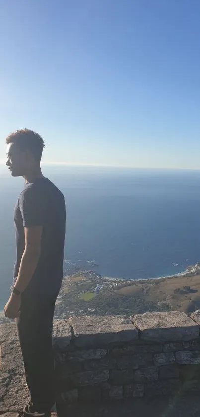 Man stands on cliff overlooking ocean under blue sky.