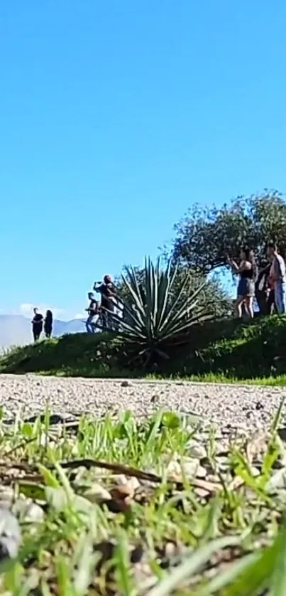 Scenic view with blue sky, greenery, and people on a dirt road.