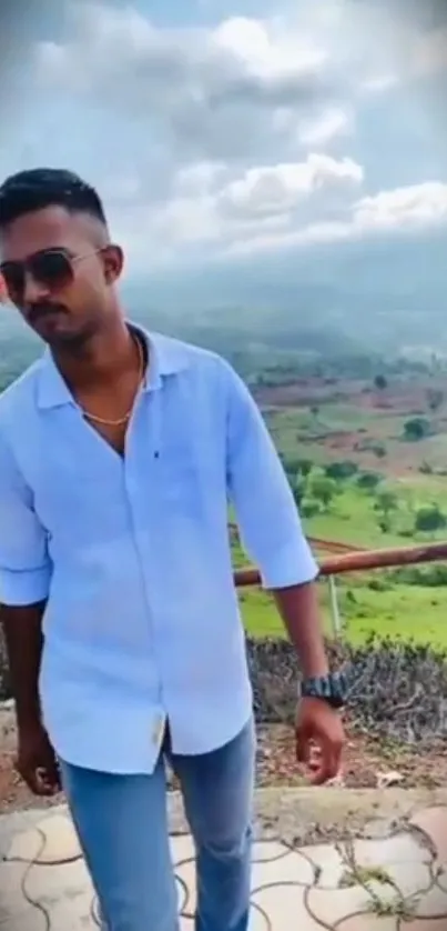 Stylish man posing in scenic outdoor landscape with green hills.