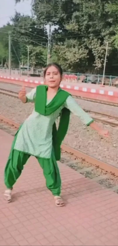 Woman dancing joyfully by railway tracks.