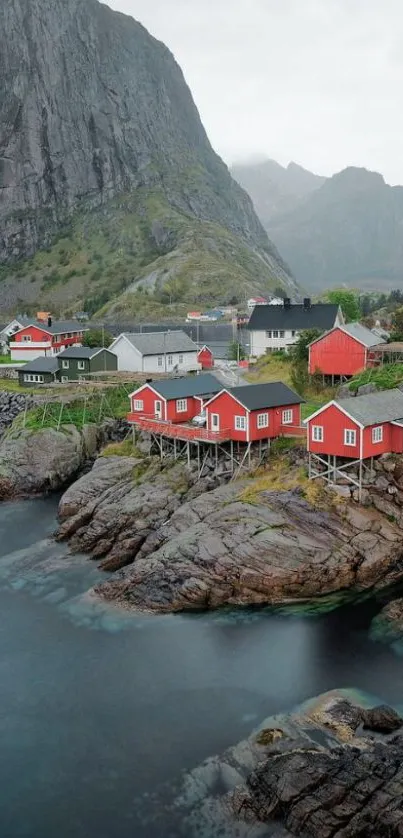 Red cabins by rocky waters with mountain backdrop.