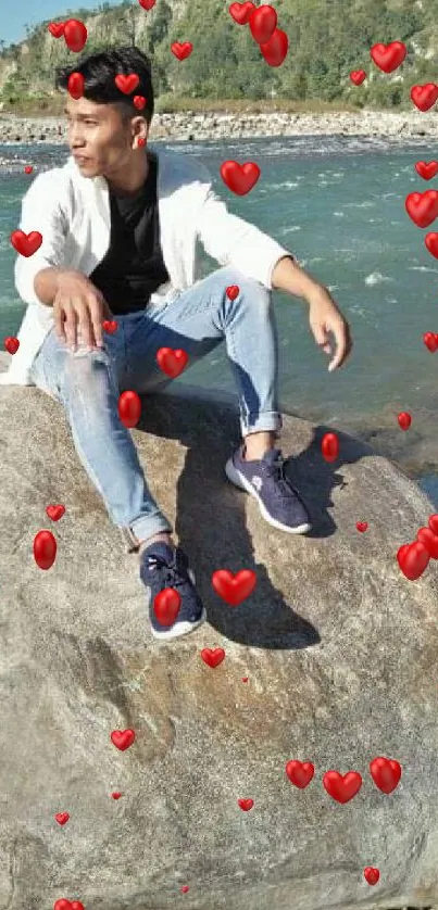 Man sitting on rock by a scenic river and mountains.