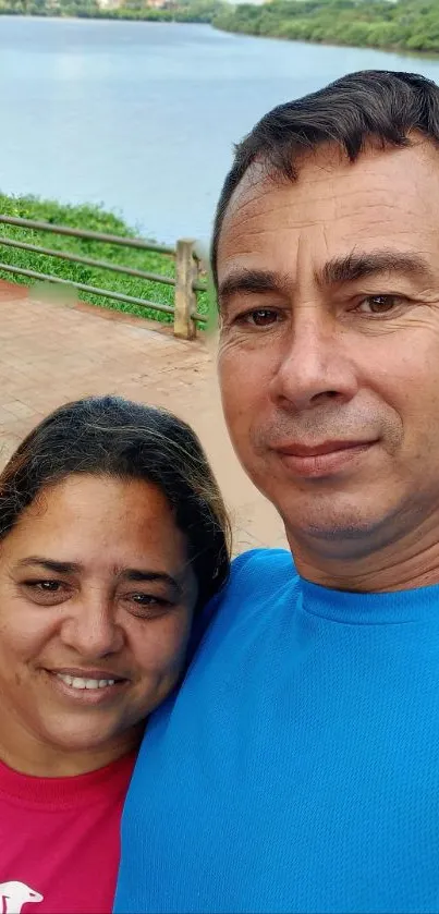 Couple's selfie by a calm riverside with lush greenery.