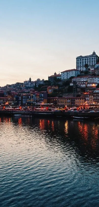 Riverside cityscape at dusk with lights reflecting on water.