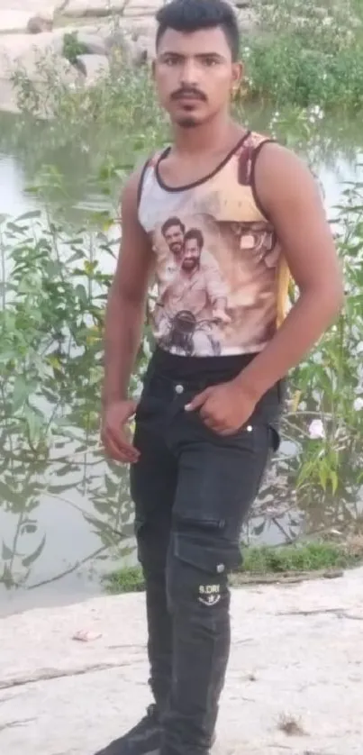 Man standing by a river with floral greenery and rocky banks.