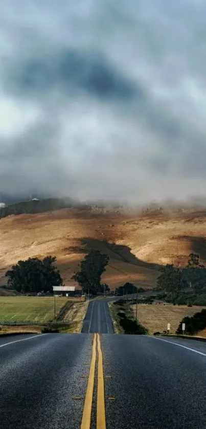 Scenic road leading to misty hills under cloudy skies.