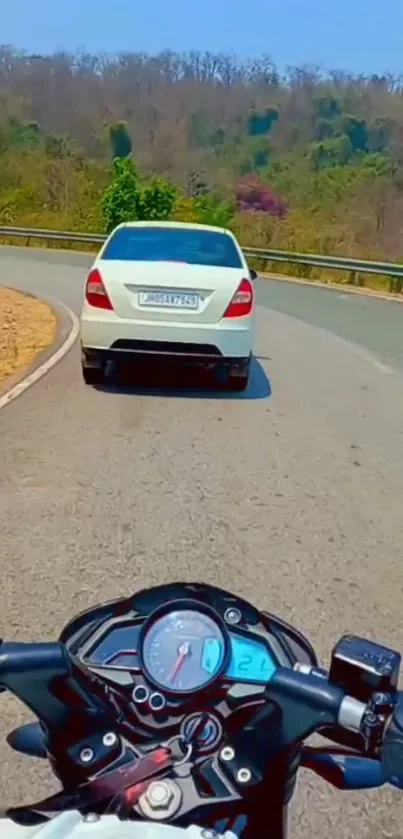 Motorbike following car on winding mountain road.