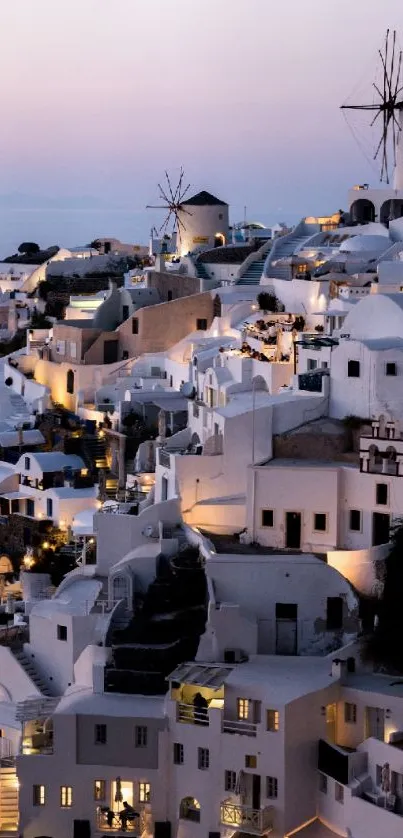 Santorini at dusk with illuminated white buildings and windmills.