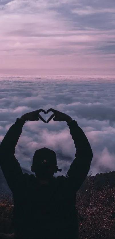 Silhouette forming a heart against a pink and purple cloudy sky over mountains.