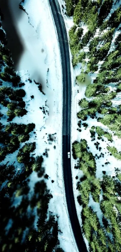 Aerial view of snowy road through green forest.