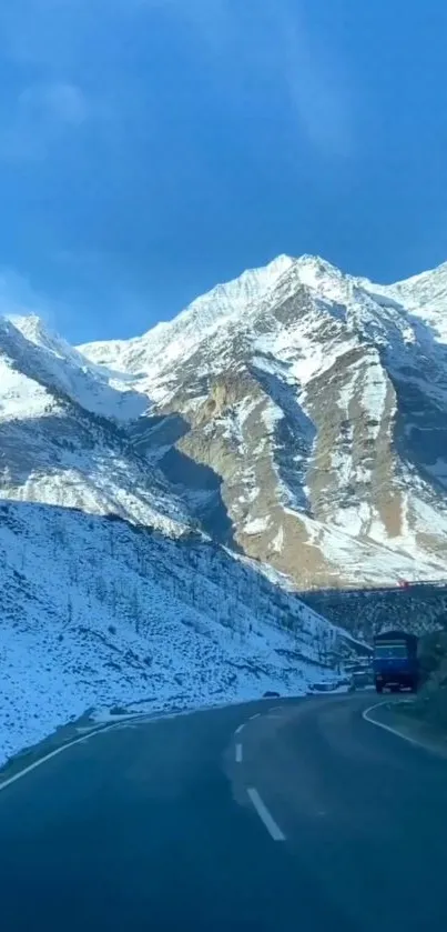 Scenic road through snow-capped mountains under a vibrant blue sky.