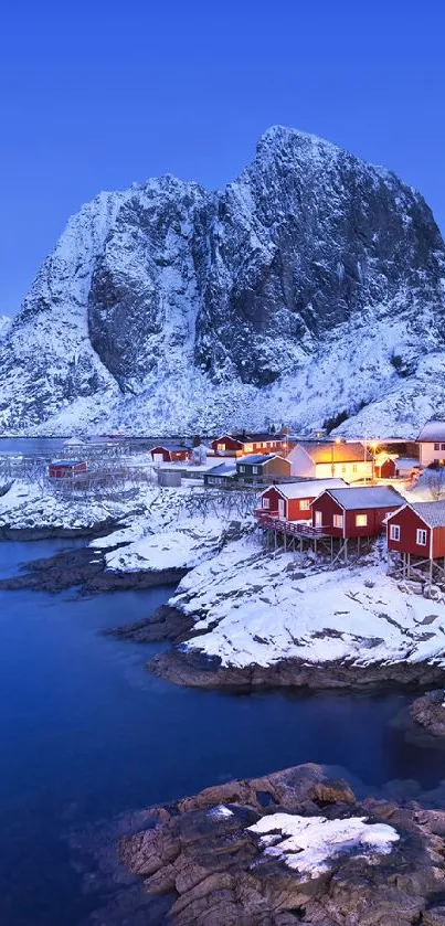 Snowy village with red cabins by the blue sea under a mountain at twilight.