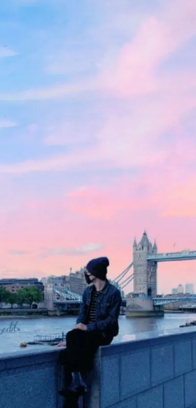 Person sitting by Tower Bridge under a pink and blue sunset sky.