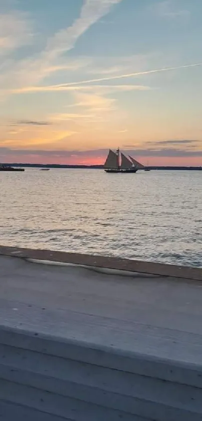 Sailboat and lighthouse at sunset on calm waters.