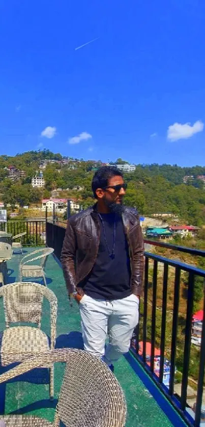 Man on scenic terrace with blue sky and green hills.