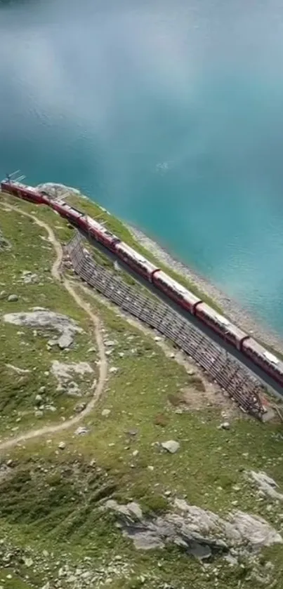 Red train passing by a turquoise lake with green hills.