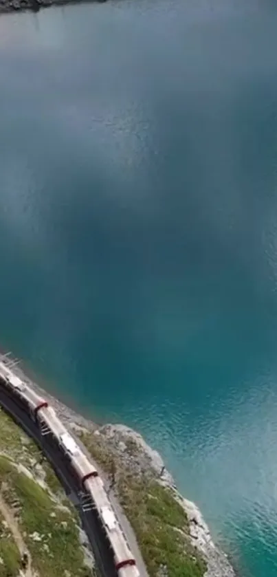 A train traveling along a turquoise lake with lush surroundings.