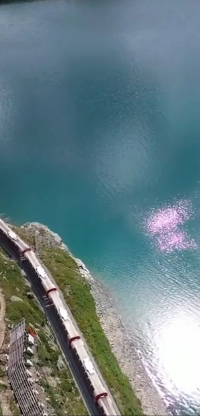 A train winding by a stunning turquoise lake under a clear sky.