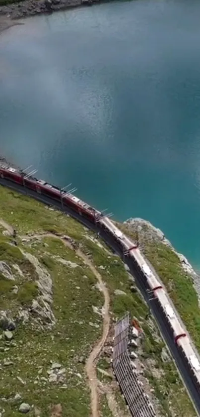 Red train curving by a turquoise lake surrounded by green landscape.