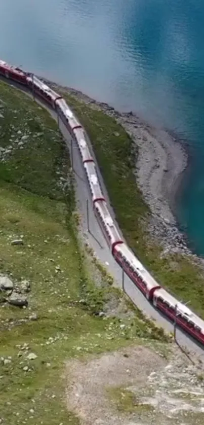 Red train traveling by a blue lake and green mountains.