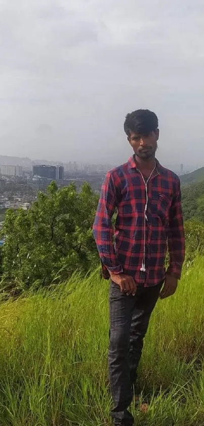 Man standing on grassy hillside with city view in background.