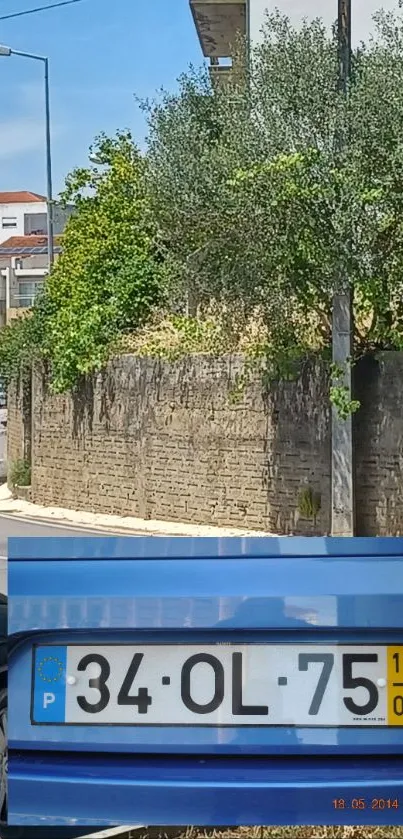 Urban street scene with stone wall and greenery under a clear sky.