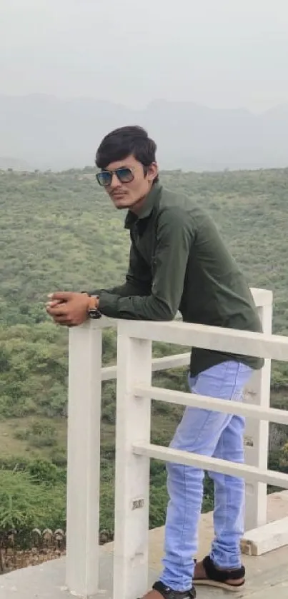 Man leaning on railing with scenic green landscape.