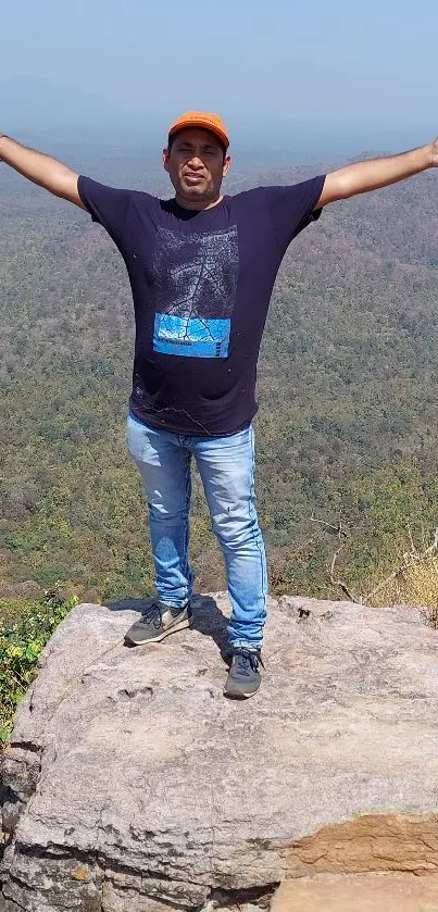 Person standing on a mountain peak overlooking a vast forest landscape.