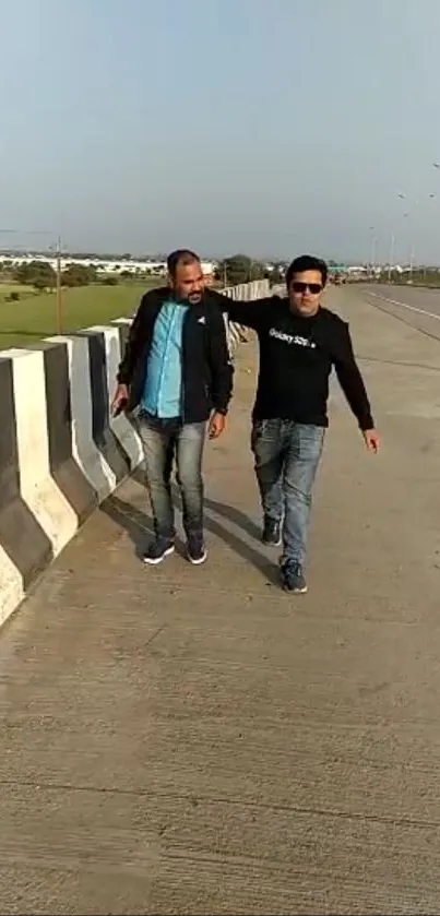 Two people walking on a scenic road under a clear blue sky.