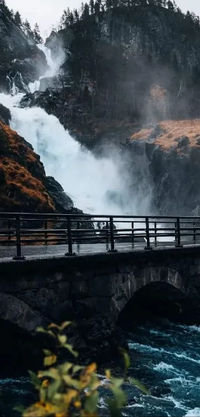 Scenic view of a waterfall behind a bridge surrounded by mountains and greenery.