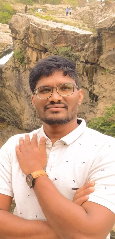 Portrait of a man in front of a scenic waterfall and rocky landscape.