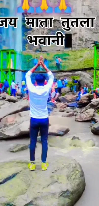 Man praying at scenic waterfall with lush greenery.