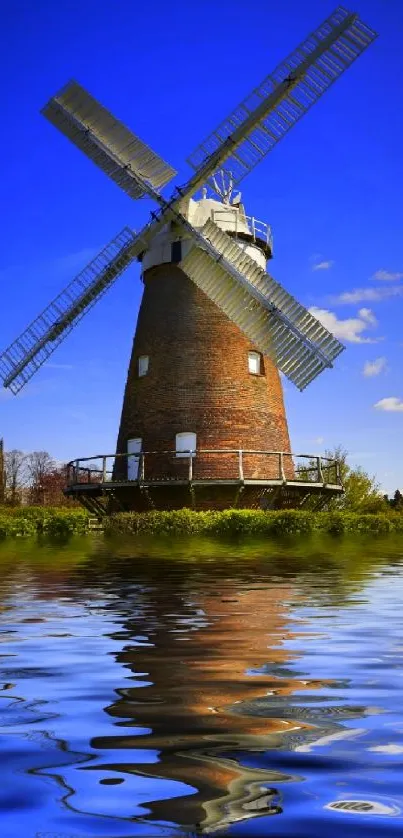 Windmill reflected in calm blue water against a bright sky.