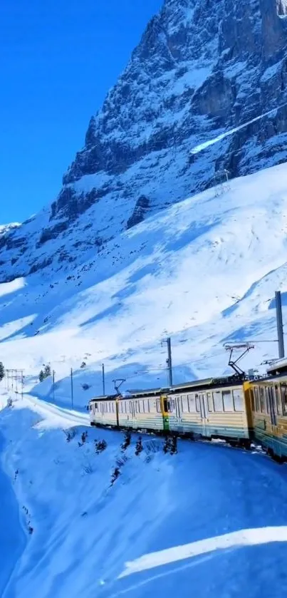 Scenic winter train journey through the snow-capped mountains under a blue sky.