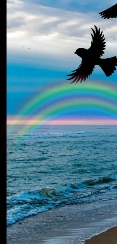 Two birds flying over a beach with a rainbow in the sky.