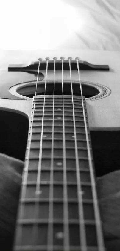 Black and white wallpaper of acoustic guitar on bed with soft lighting.