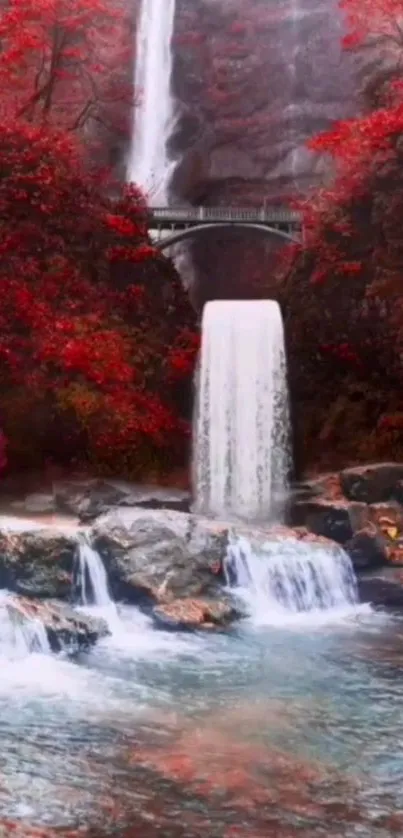 Waterfall amidst vibrant red autumn foliage under a bridge.