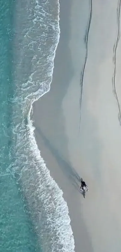 Aerial view of a beach with a lone person, waves, and soft sand.